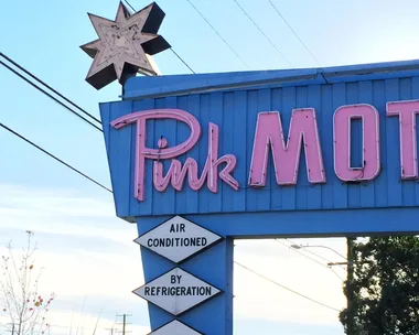 Sign of the Pink Motel with retro-style neon letters in pink and blue background. Sign shows "Air Conditioned By Refrigeration" and "TV."