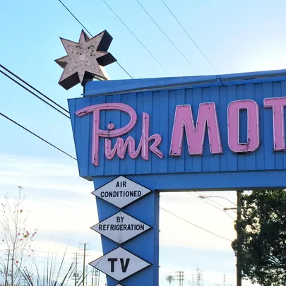 Sign of the Pink Motel with retro-style neon letters in pink and blue background. Sign shows "Air Conditioned By Refrigeration" and "TV."