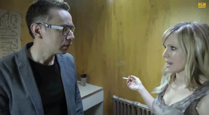 Fred Armisen and Kristen Bell reenact a scene from "Birdman," standing in a dimly lit room with Bell holding a cigarette.