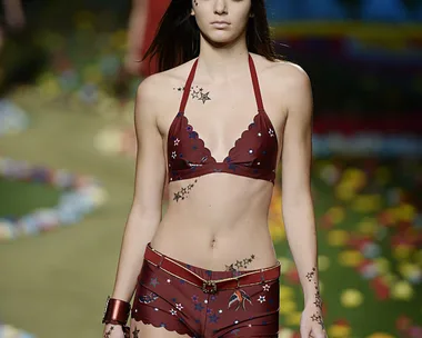 Model wearing a red bikini with star tattoos on the runway at Tommy Hilfiger AW15 show.
