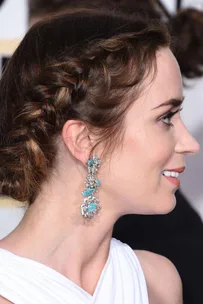 Woman with side braid hairstyle and intricate earrings, smiling at an event.