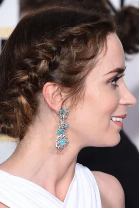 Woman with side braid hairstyle and intricate earrings, smiling at an event.