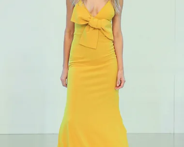 Model in a yellow gown with a large bow on the front, walking on the runway.