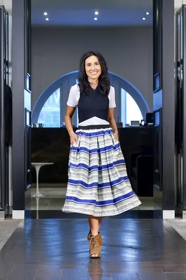 Woman in a striped midi skirt with hands in pockets, smiling and walking indoors.