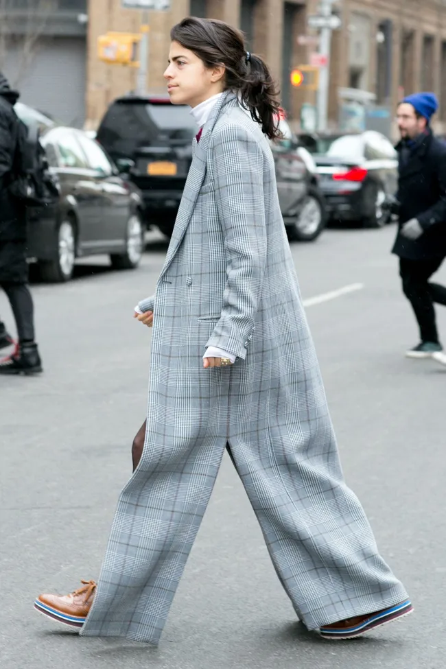 Person in oversized plaid suit and platform shoes, walking on city street.