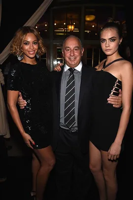 Three people posing together at an event; two women in black dresses and a man in a suit in the middle.