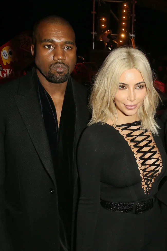 Two individuals in stylish black outfits seated at Givenchy front row event, with lights in the background.