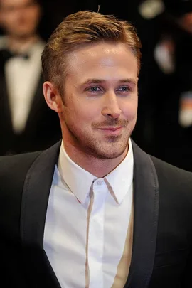 Ryan Gosling dressed in a black suit and white shirt at a formal event. Text: ryan-gosling-joins-the-hot-tattooed-dad-club-3584.