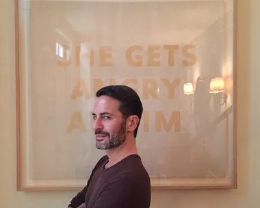 Man posing with a framed art piece behind him. The text on the art reads "SHE GETS ANGRY AT HIM."