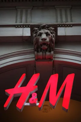 H&M sign in red below an architectural lion head sculpture on a building facade.