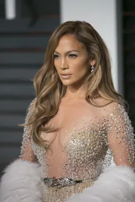 Jennifer Lopez attending an event, wearing a sparkling, low-cut gown and earrings, with long, wavy hair styled.