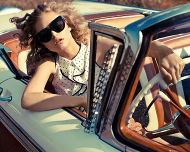 Woman with sunglasses in polka dot dress driving a vintage car.