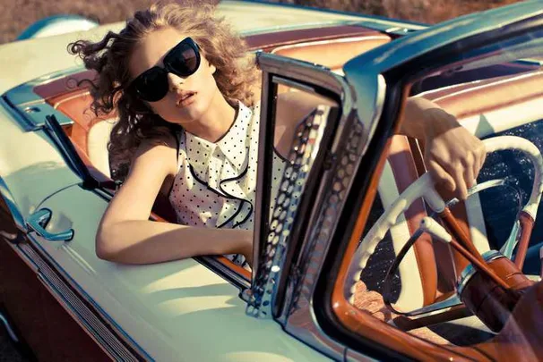 Woman with sunglasses in polka dot dress driving a vintage car.