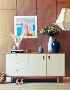 Modern sideboard with abstract artwork, decorative vases, books, and a hanging lamp in a stylish living space.