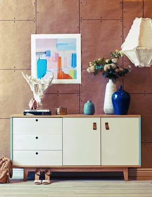 Modern sideboard with abstract artwork, decorative vases, books, and a hanging lamp in a stylish living space.