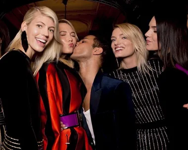 Models pose playfully with a designer wearing stylish outfits at a fashion event.