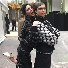 Two women in stylish outfits posing playfully at a fashion event, one smiling and the other serious.