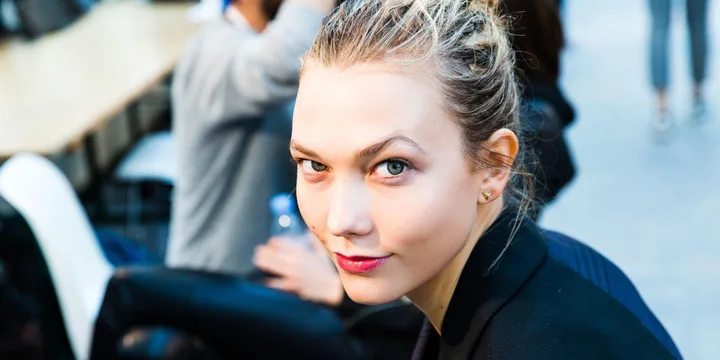 Woman with blonde hair tied back, wearing a black top, looking at the camera with a slight smile in an indoor setting.