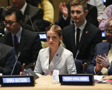 Emma Watson at a United Nations event, sitting between Ban Ki-moon and President General Assembly, with nameplates visible.