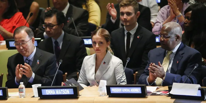 Emma Watson at a United Nations event, sitting between Ban Ki-moon and President General Assembly, with nameplates visible.