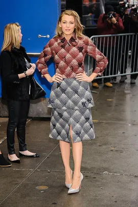 Blake Lively in plaid top and skirt, posing outside on a rainy day with photographers in the background.