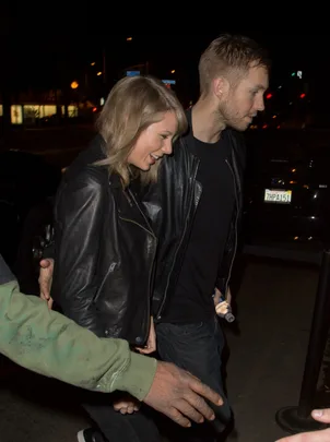 A man and a woman, both wearing black jackets, walking hand-in-hand at night.