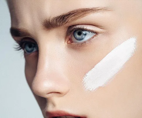 Close-up of a woman's face with a swatch of white cream applied to her cheek.