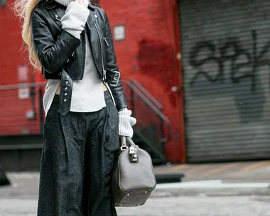 Woman in winter street style: leather jacket, turtleneck, wide-leg pants, holding bag, in city setting.