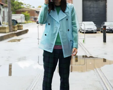 Person in a blue coat takes a photo outside on a rainy day with water puddles on the ground.