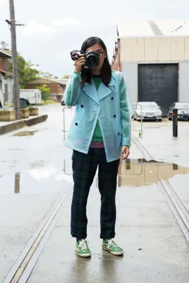 Person in a blue coat takes a photo outside on a rainy day with water puddles on the ground.