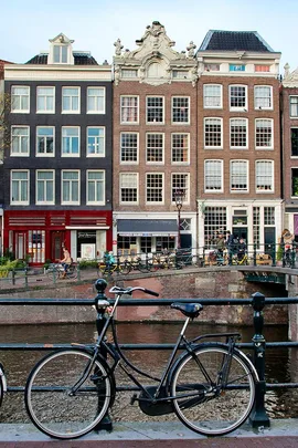 A bicycle parked by a canal in Amsterdam, with traditional Dutch houses in the background.