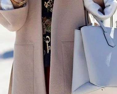 Person holding a smartphone and a white handbag, wearing a beige coat.