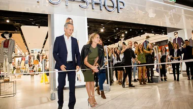 A woman cuts the ribbon at the TOPSHOP store opening in Westfield Miranda, with a man and a cheering crowd.