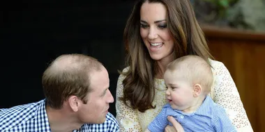 A man and a woman smiling at each other while the woman holds a baby in her arms.