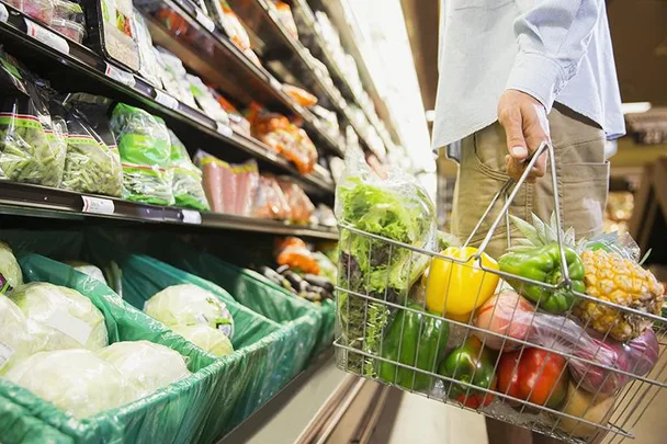 Man shopping for fresh produce at grocery store, holding basket of vegetables and fruits.