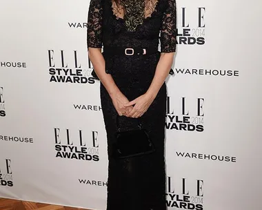 A woman in a black lace dress posing at the ELLE Style Awards 2014, with a backdrop featuring "WAREHOUSE."