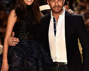 Fashion designer with model in black dress at Australian Fashion Week runway show.