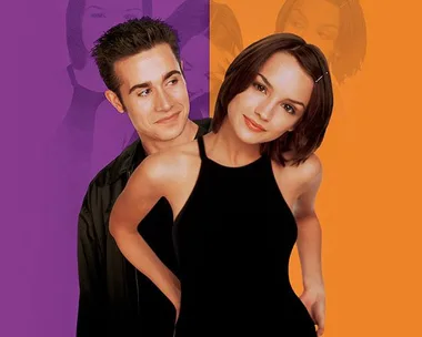 A young man and woman from "She's All That" stand close together with a colorful background.