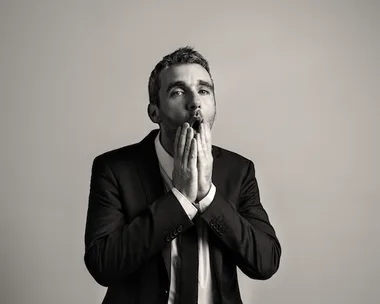 Alt text: "A man in a suit looks surprised with hands near his mouth in a black and white photograph."