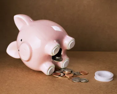 A pink piggy bank laying on its side with coins spilling out onto the table. The stopper is removed.