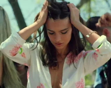 A woman in a floral top dances with her hands on her head, surrounded by others outdoors.