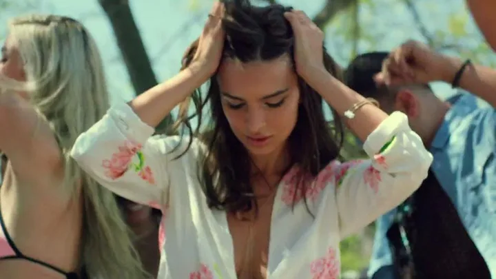 A woman in a floral top dances with her hands on her head, surrounded by others outdoors.