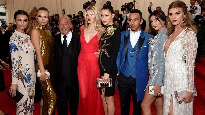 A group of seven models and a man, dressed in elegant attire, posing on the red carpet at the Met Gala.