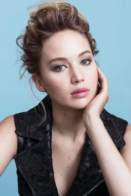 Jennifer Lawrence in a Dior campaign with an updo hairstyle, wearing a black outfit, posing with her hand on her cheek.