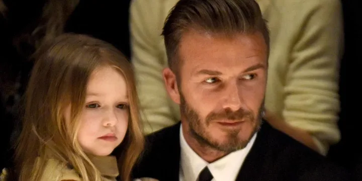 David Beckham and daughter Harper at an event, sitting closely and watching attentively.