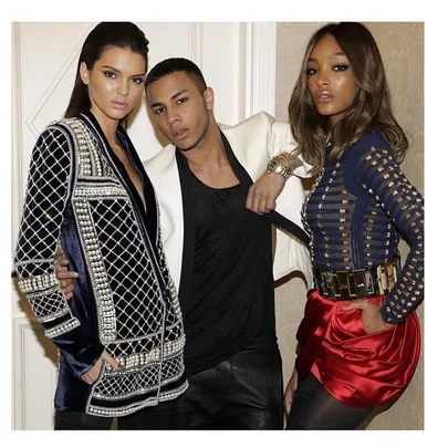 Three fashion models wearing Balmain clothing posing together prominently display stylish jackets and a red skirt.