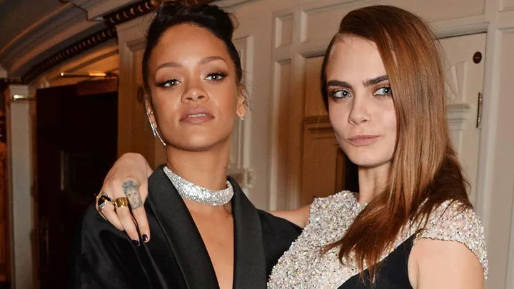 Two women posing together, one with a high bun and black attire, the other with straight hair and a bejeweled dress.