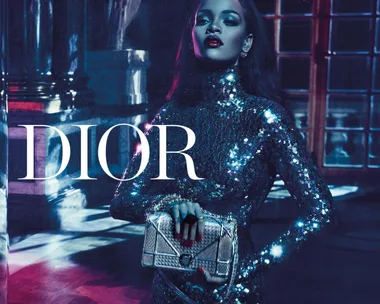 Rihanna in a sparkling, blue dress holding a Dior handbag, featured in the Dior "Secret Garden IV Versailles" campaign.