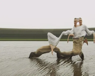 Two distorted, mirrored figures walk on water, blending into each other with a blurred background in an abstract photograph.