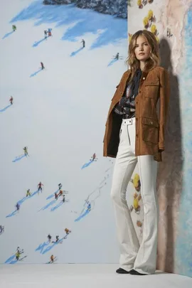 Model in suede jacket and white flared pants with a ski-themed backdrop from Resort 2016 fashion collection.